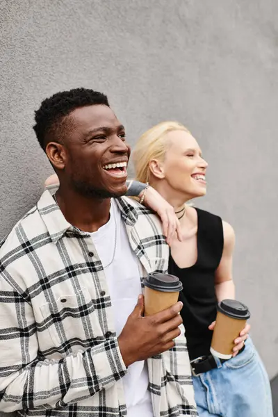 Multicultural couple enjoying coffee together on an urban street near a grey building. — Stock Photo