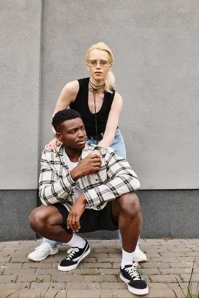 Un uomo si inginocchia accanto a una donna, mostrando amore e compassione, contro un edificio grigio su una strada urbana. — Foto stock