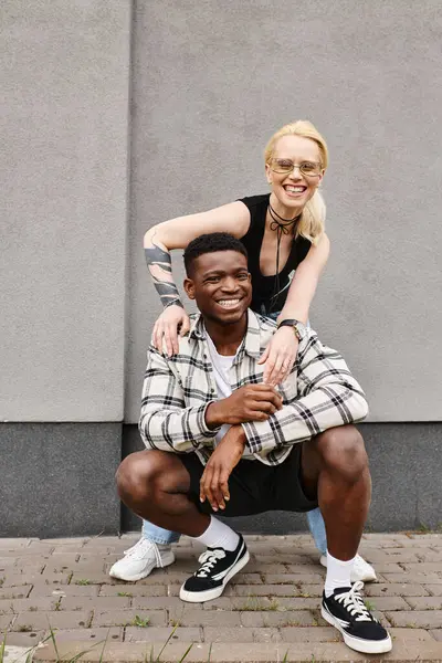 Ein fröhlicher multikultureller Freund und seine Freundin posieren gemeinsam auf einer städtischen Straße in der Nähe eines grauen Gebäudes und lächeln in die Kamera. — Stockfoto