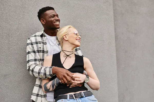 Un couple multiculturel, un homme et une femme se tiennent heureux ensemble dans une rue urbaine près d'un bâtiment gris. — Photo de stock