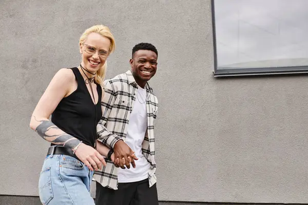Ein glückliches multikulturelles Paar, ein Mann und eine Frau, stehen zusammen auf einer städtischen Straße in der Nähe eines grauen Gebäudes. — Stockfoto