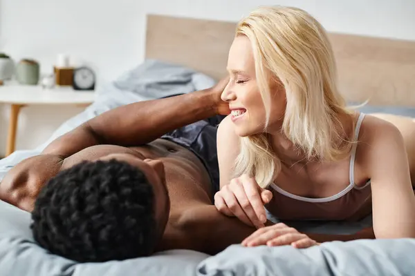 A sensual moment captured as a multicultural man and woman embrace intimately while laying on a bed at home. — Stock Photo
