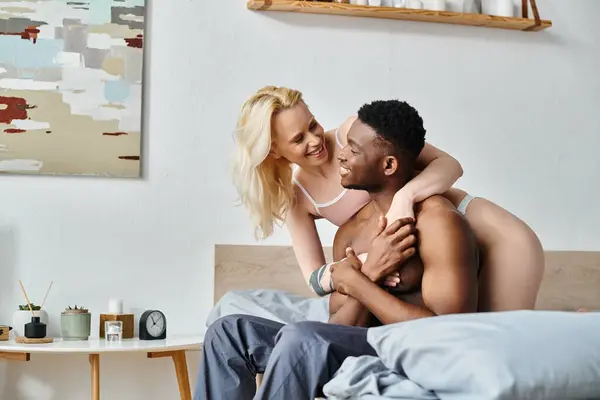 A sexy multicultural boyfriend and girlfriend cuddle lovingly on a cozy bed in a home setting. — Stock Photo