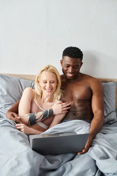 Un fidanzato multiculturale e una fidanzata godono di un momento di intimità, sdraiati comodamente a letto insieme. — Foto stock