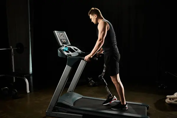 Ein Mann mit Beinprothese übt auf einem Laufband in der schwach beleuchteten Turnhalle. — Stockfoto