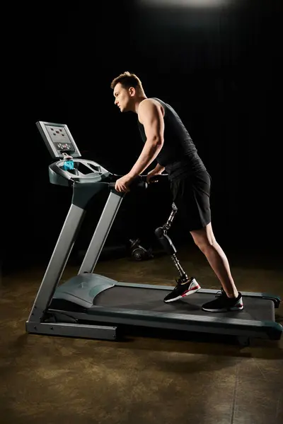 A man with a prosthetic leg runs on a treadmill in a dimly lit room, showing determination and strength in his workout. - foto de stock