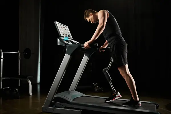 Un hombre con una pierna protésica trabaja en una cinta de correr en un gimnasio oscuro - foto de stock