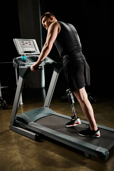 A disabled man with a prosthetic leg exercises on a treadmill in a dimly lit room. — Stock Photo