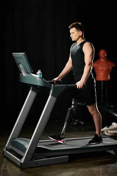 A man with a prosthetic leg stands on a treadmill in a dark room, pushing himself to keep going. - foto de stock