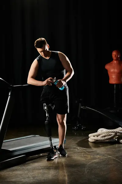 Un uomo, con una gamba protesica, si trova su un tapis roulant in una stanza poco illuminata, concentrato sulla sua routine di allenamento.. — Foto stock