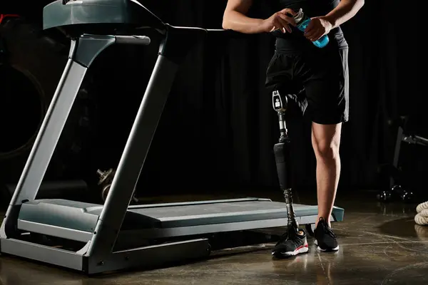 A disabled man with a prosthetic leg is standing on a treadmill in a dark room, focused on his workout routine. — Stock Photo