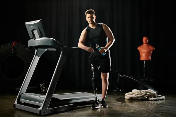 Ein behinderter Mann mit Beinprothese steht auf einem Laufband in einem dunklen Raum und konzentriert sich auf sein Workout. — Stockfoto