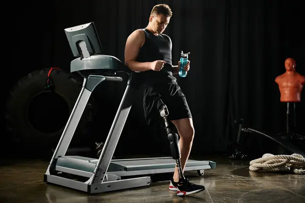 A disabled man with a prosthetic leg stands on a treadmill, holding a water bottle while working out in a gym. — Stock Photo