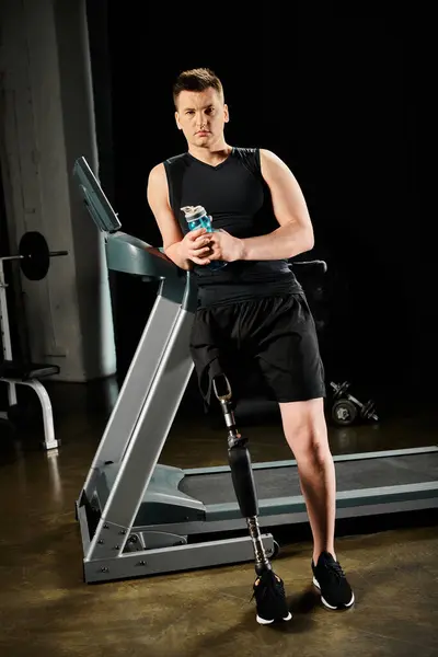 Un uomo sta su un tapis roulant, tenendo un drink in mano mentre si allena in palestra con una gamba protesica. — Foto stock
