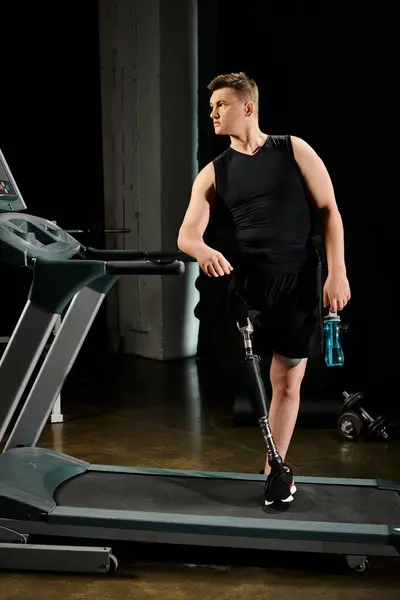 Un hombre discapacitado con una pierna protésica está trotando en una cinta de correr mientras sostiene una botella de agua. - foto de stock
