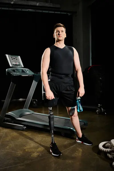 Un homme avec une prothèse de jambe debout sur un tapis roulant dans une pièce faiblement éclairée, activement engagé dans une routine d'entraînement. — Photo de stock