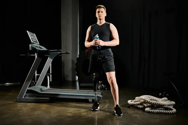 Un hombre con una pierna protésica se para frente a una cinta de correr, listo para entrenar en el gimnasio. - foto de stock