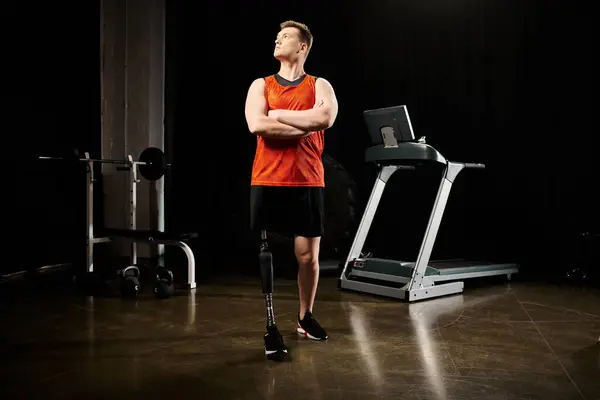 Un hombre discapacitado determinado con una pierna protésica se para con confianza frente a una cinta de correr en un gimnasio, listo para hacer ejercicio.. - foto de stock