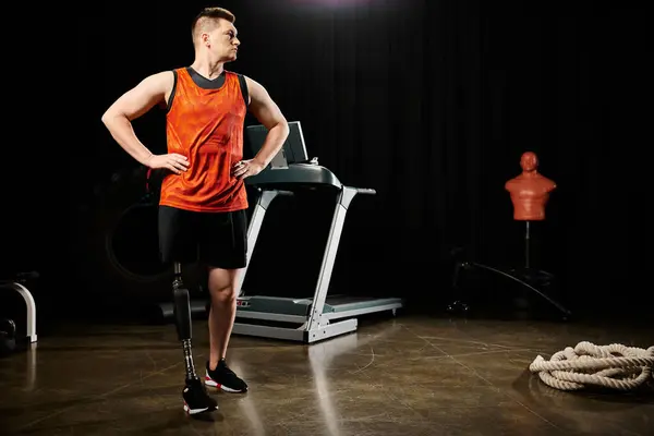 Un hombre discapacitado con una pierna protésica está de pie con confianza frente a una cinta de correr en un gimnasio, listo para embarcarse en su entrenamiento. - foto de stock