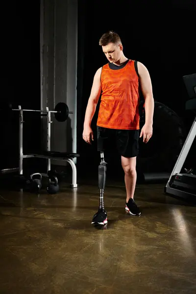 Un hombre con una pierna protésica, de pie en un gimnasio rodeado de equipo de ejercicio. - foto de stock