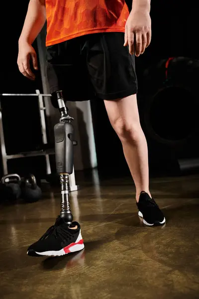 Un uomo con una gamba protesica in camicia arancione e pantaloncini neri in piedi accanto a un bianco e nero. — Foto stock