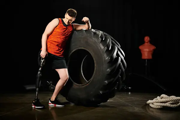 Un uomo con una gamba protesica sta orgogliosamente accanto a un enorme pneumatico, mostrando forza e perseveranza.. — Foto stock