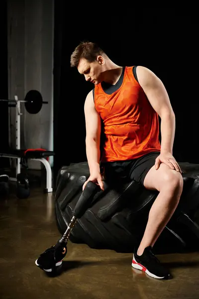 Ein behinderter Mann mit Beinprothese sitzt auf einem Reifen in einer Turnhalle und demonstriert Widerstandskraft und Entschlossenheit. — Stockfoto