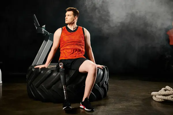 Ein Mann mit Beinprothese sitzt selbstbewusst auf einem kolossalen Reifen und demonstriert Kraft und Gleichgewicht in einer unkonventionellen Trainingsroutine. — Stockfoto