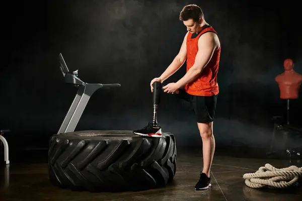 A disabled man with a prosthetic leg stands next to a tire on top of a table, displaying strength and balance. — Stock Photo