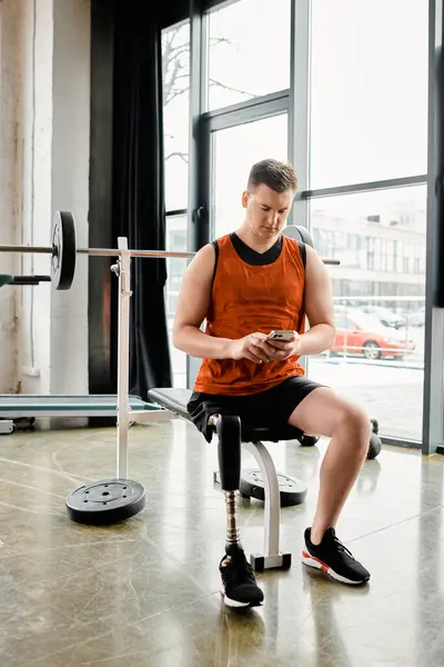 Un homme avec une prothèse de jambe, assis dans une chaise, absorbé dans l'écran de son téléphone portable. — Photo de stock
