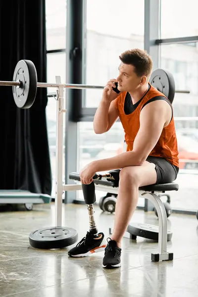 A man with a prosthetic leg sits on a bench, next to a barbell in a gym. - foto de stock