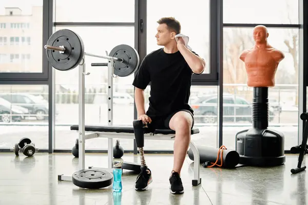 Ein behinderter Mann mit Beinprothese sitzt auf einer Bank in einem Fitnessstudio und ruht sich während seiner Trainingseinheit aus.. — Stockfoto
