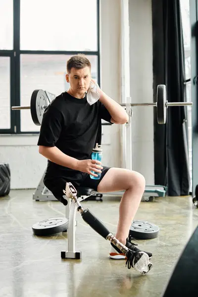 Un hombre con una pierna protésica se sienta pacíficamente en un banco, sosteniendo una botella de agua. - foto de stock