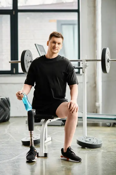 Ein entschlossener Mann mit Beinprothese sitzt in einem Stuhl neben einer Langhantel in einem Fitnessstudio und demonstriert Stärke und Widerstandskraft. — Stockfoto
