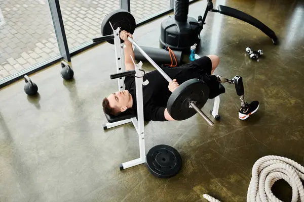 Un uomo disabile con una gamba protesica sdraiato tranquillamente su una panchina in palestra, mostrando forza e resilienza nella sua routine di allenamento. — Foto stock