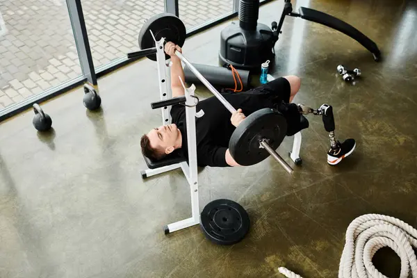 Un uomo disabile con una gamba protesica sdraiato tranquillamente su una panchina in palestra, mostrando forza e resilienza nella sua routine di allenamento. — Foto stock