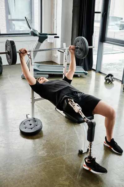 Um homem, com uma perna protética, está realizando um exercício de supino com uma barra no ginásio. — Fotografia de Stock