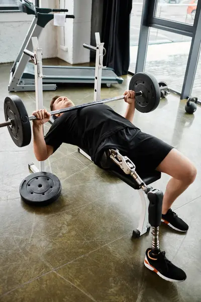 Ein Mann mit Beinprothese führt in einem Fitnessstudio einen Bankdrücken mit einer Langhantel durch. — Stockfoto