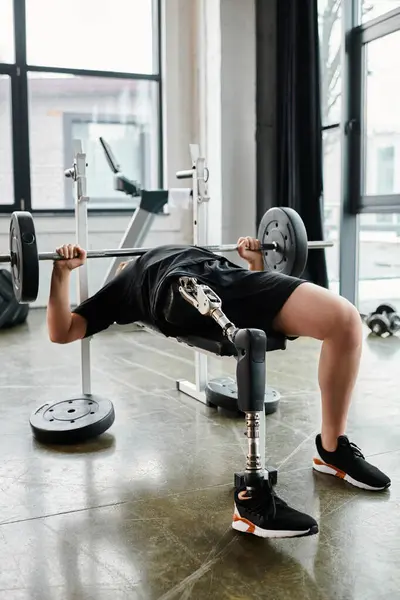 A man, with a prosthetic leg, lifting a barbell while doing a bench press in a gym. - foto de stock