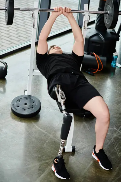 A disabled man with a prosthetic leg wearing a black shirt performs a barbell squat in a gym. — Stock Photo