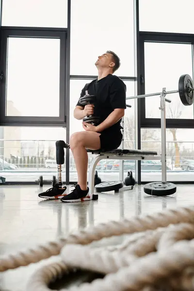 A disabled man with a prosthetic leg finding solace while sitting on a bench in a gym. — Stock Photo