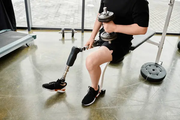 Un hombre con una pierna protésica sentado encima de un banco, sosteniendo una mancuerna para un entrenamiento. - foto de stock
