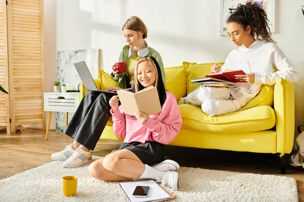 Разнообразная группа девочек-подростков, сидящих рядом на ярко-желтом диване, сосредоточена на изучении и обмене моментами дружбы и образования. — стоковое фото
