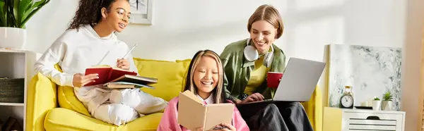 A group of diverse teenage girls are sitting and studying together on a yellow couch in a cozy setting. — Stock Photo
