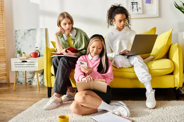 Three diverse teenage girls engrossed in studying together on a couch while looking at a book. — Stock Photo