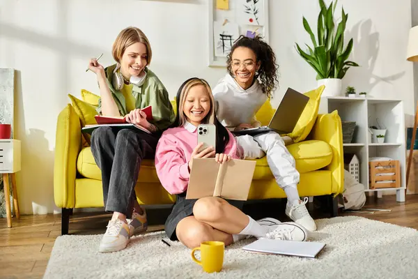 Three teenage girls of different races sit together on a yellow couch. They appear to be studying and enjoying each others company. — Stock Photo
