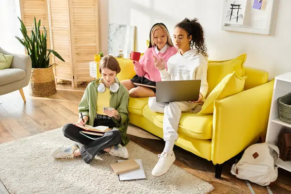 Grupo de meninas adolescentes inter-raciais felizes estudando juntas em um dia ensolarado, colando livros em um sofá amarelo brilhante. — Fotografia de Stock