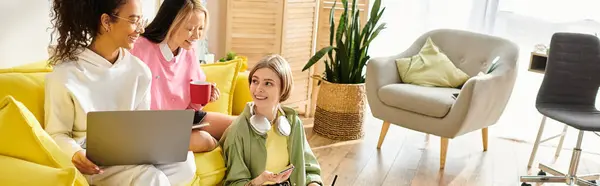 Un grupo diverso de mujeres jóvenes participan en el aprendizaje y la camaradería mientras están sentadas en un sofá amarillo vibrante. - foto de stock