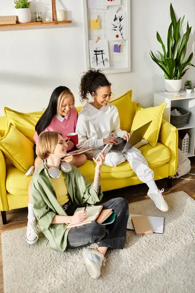 A diverse group of girls laughing while sitting on top of a bright yellow couch inside a cozy room. — Stock Photo