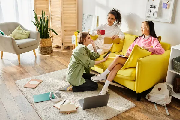 Мультикультурные девочки-подростки связываются на уютном желтом диване, делятся историями и учебными материалами для домашнего обучения. — стоковое фото